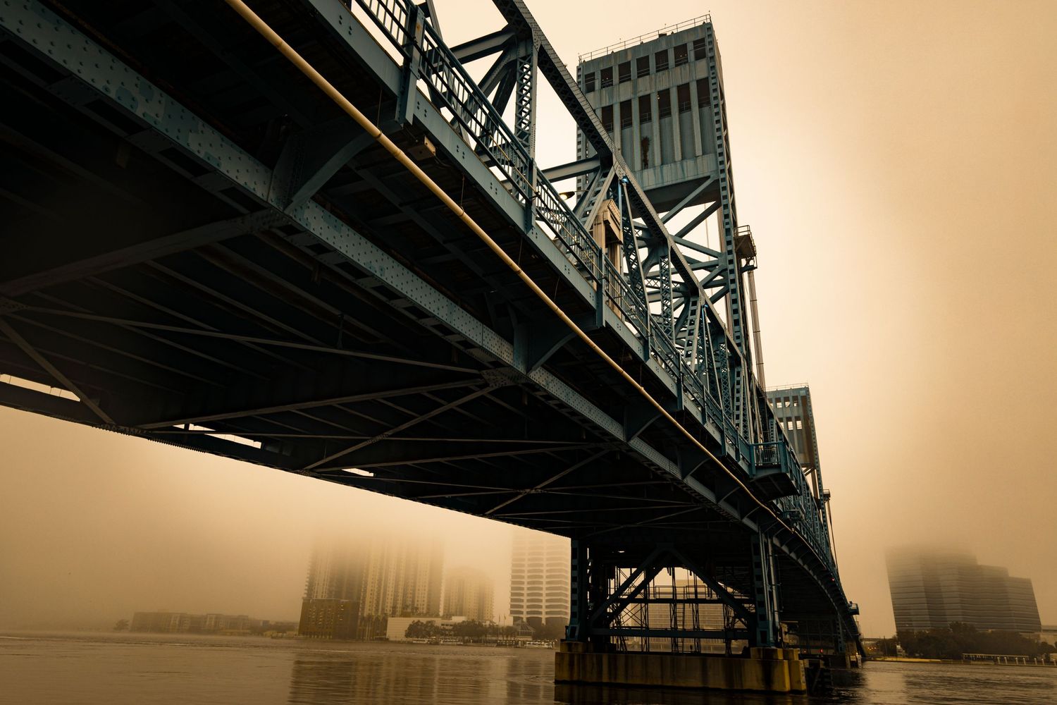 Dramatic sepia-toned view of a steel bridge structure spanning across a foggy river.