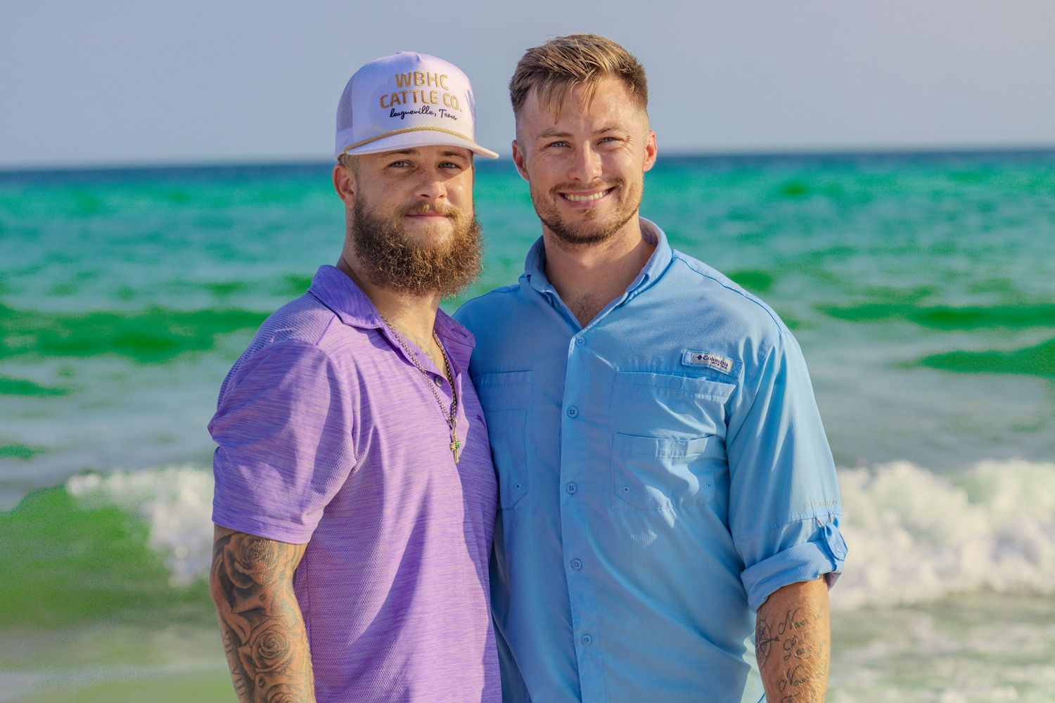 Two friends enjoying a sunny day at the beach with emerald green waters in the background.