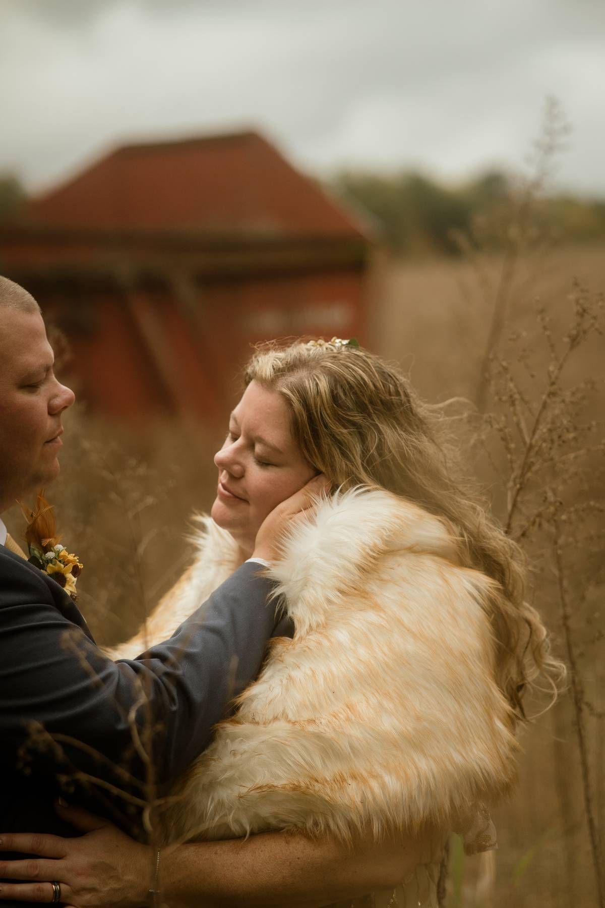 a groom holding his brides cheek as he stares loving at her while they stand in a fall field
