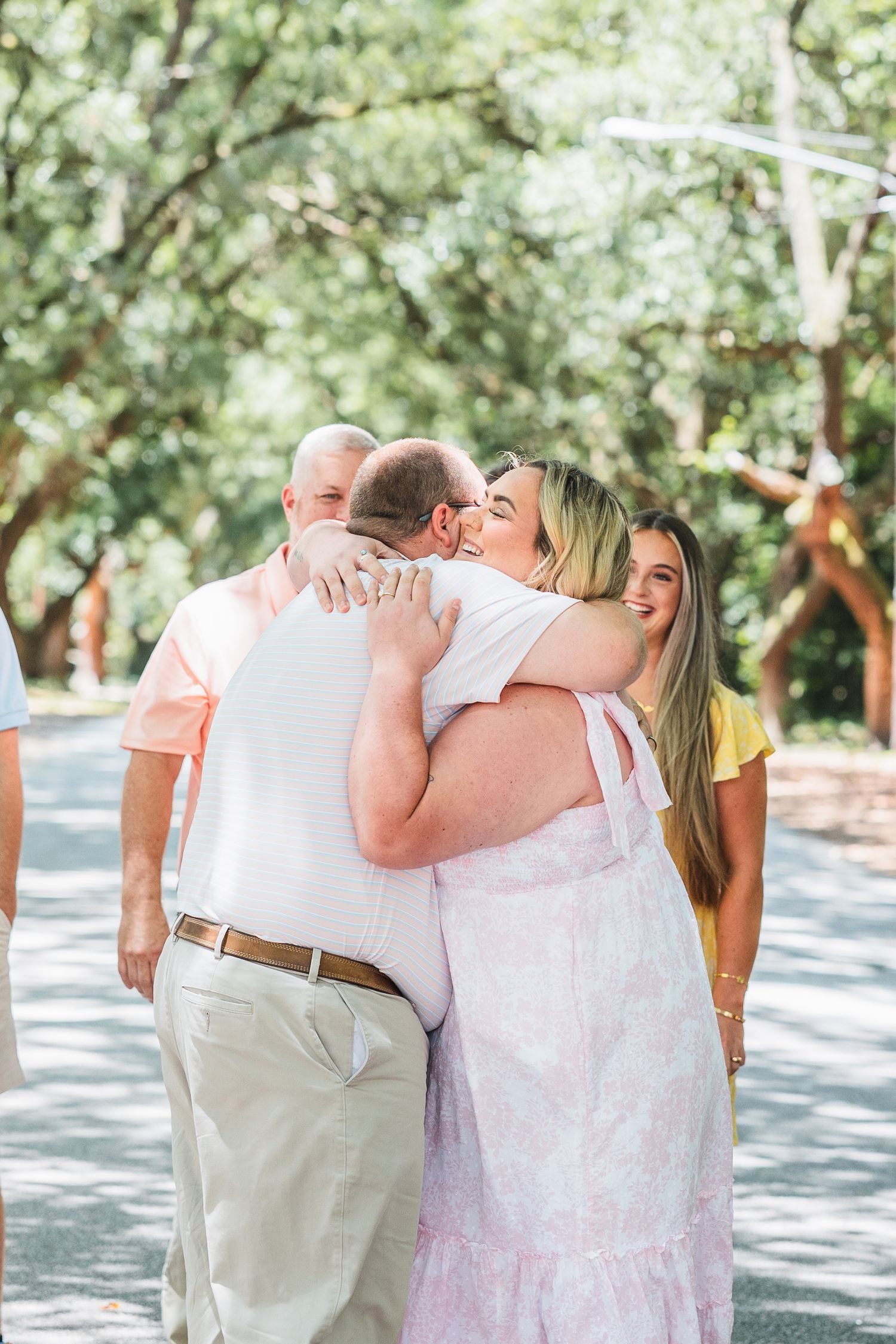 Emotional embraces shared between family members on a tree-lined path.