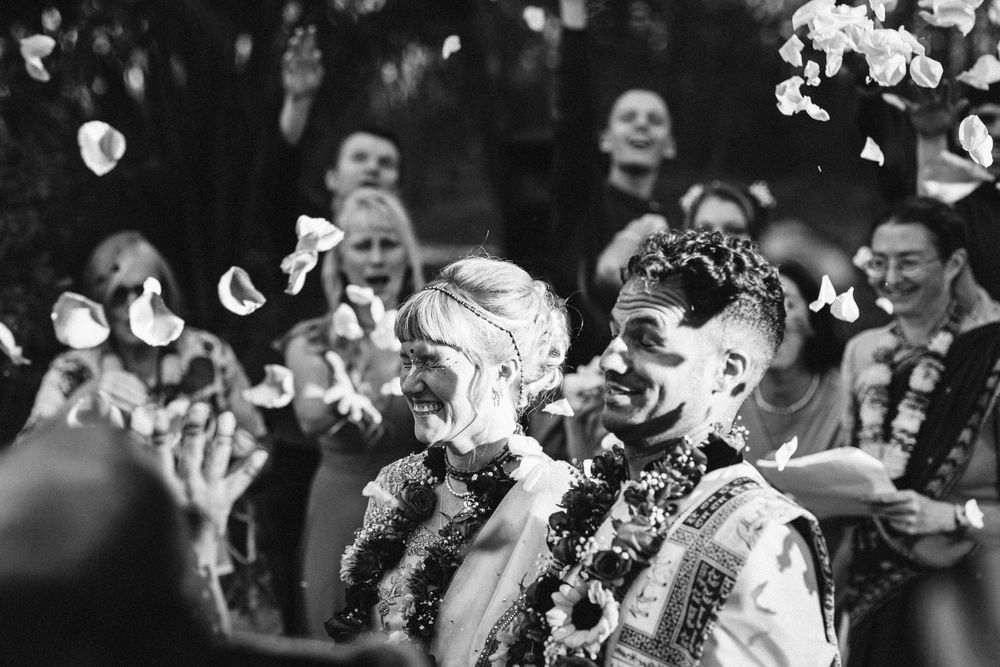 Black and white photo of a joyful couple showered with flower petals at their wedding celebration.