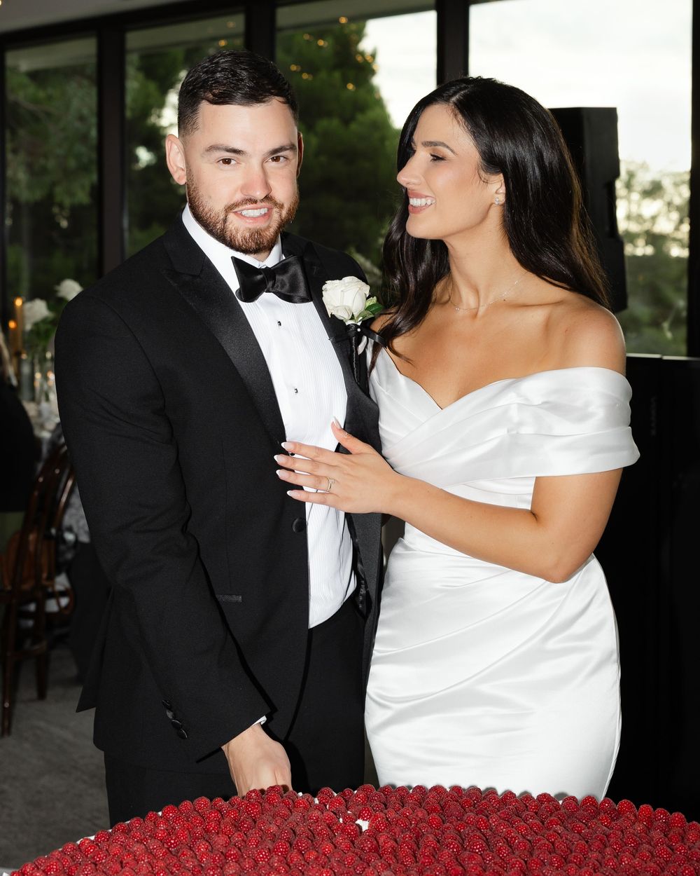 Bride in white gown and groom in tuxedo cutting wedding cake.