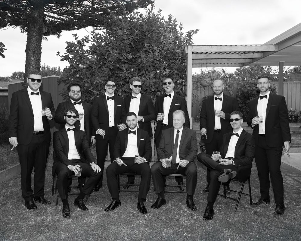 Black and white photo of groomsmen in tuxedos posing outdoors.