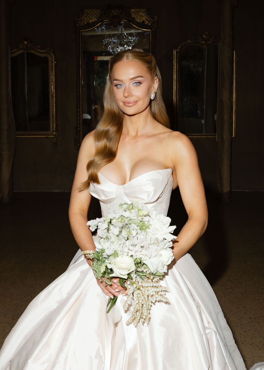 White strapless wedding gown with floral bouquet photographed in an ornate indoor setting.