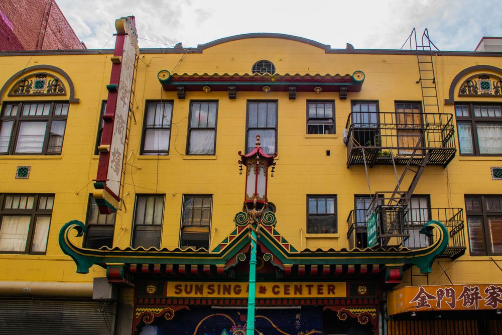Yellow building with Chinese architectural elements and fire escapes in urban setting.