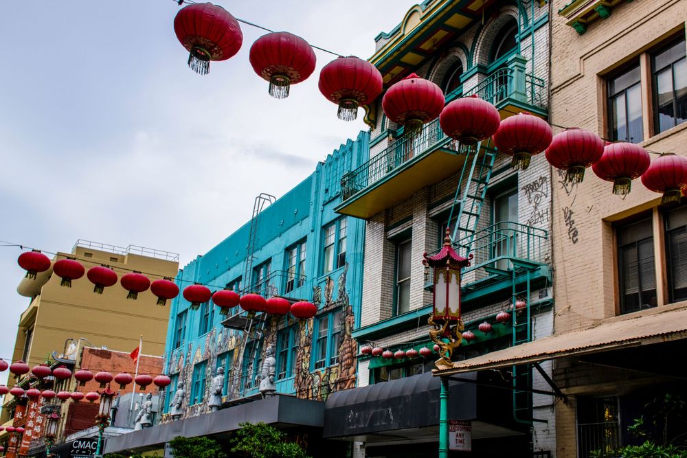 Row of red Chinese lanterns hanging above turquoise building facades.