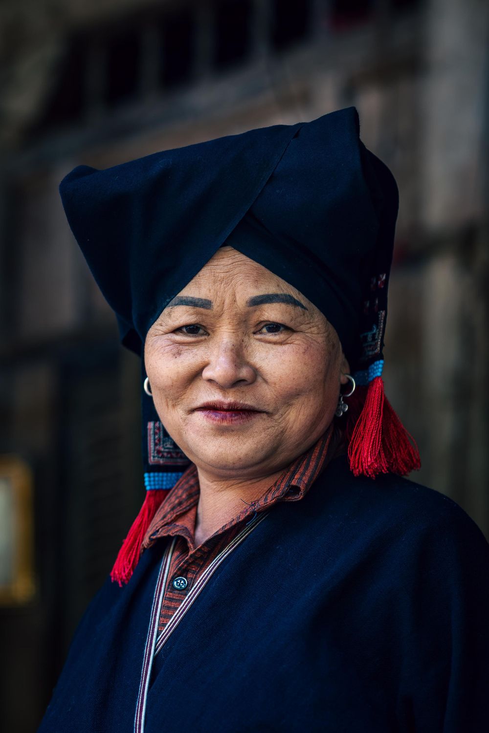 Traditional dress with dark headpiece and red tassels in cultural setting.