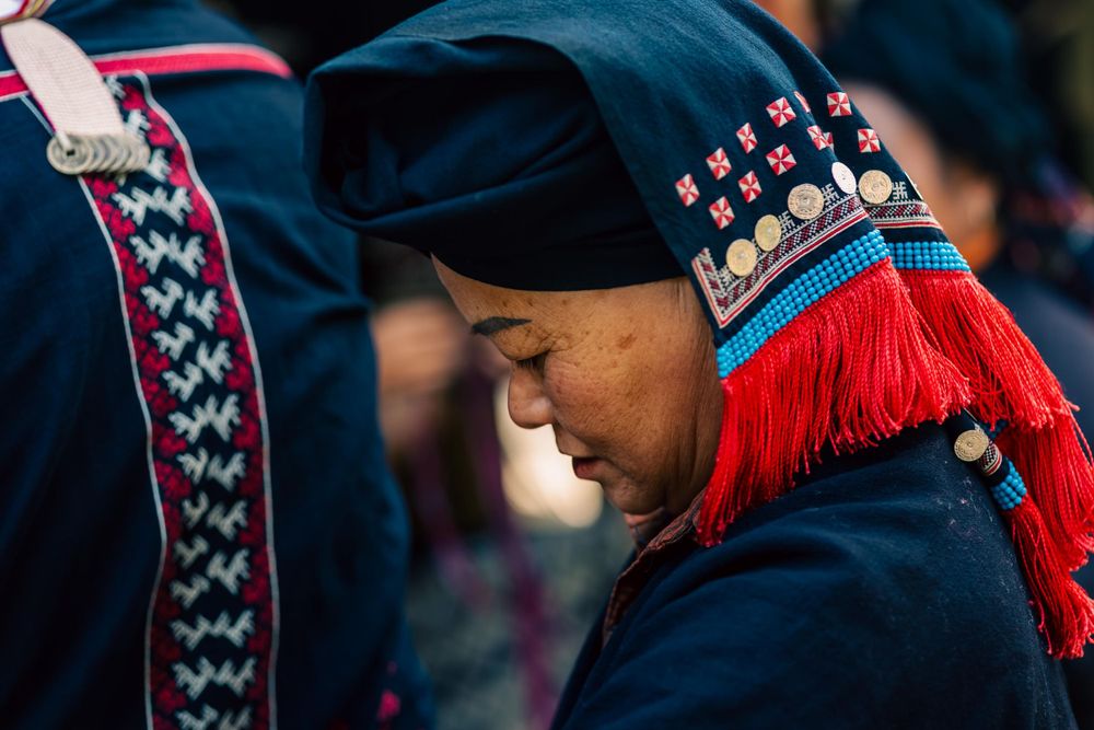 Traditional clothing with vibrant red tassels and blue embroidered details against a dark background.