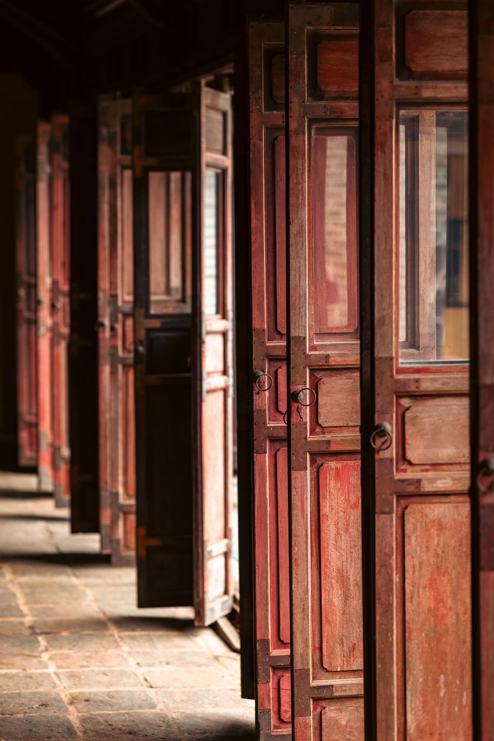 Row of weathered red wooden doors in traditional Asian temple corridor.