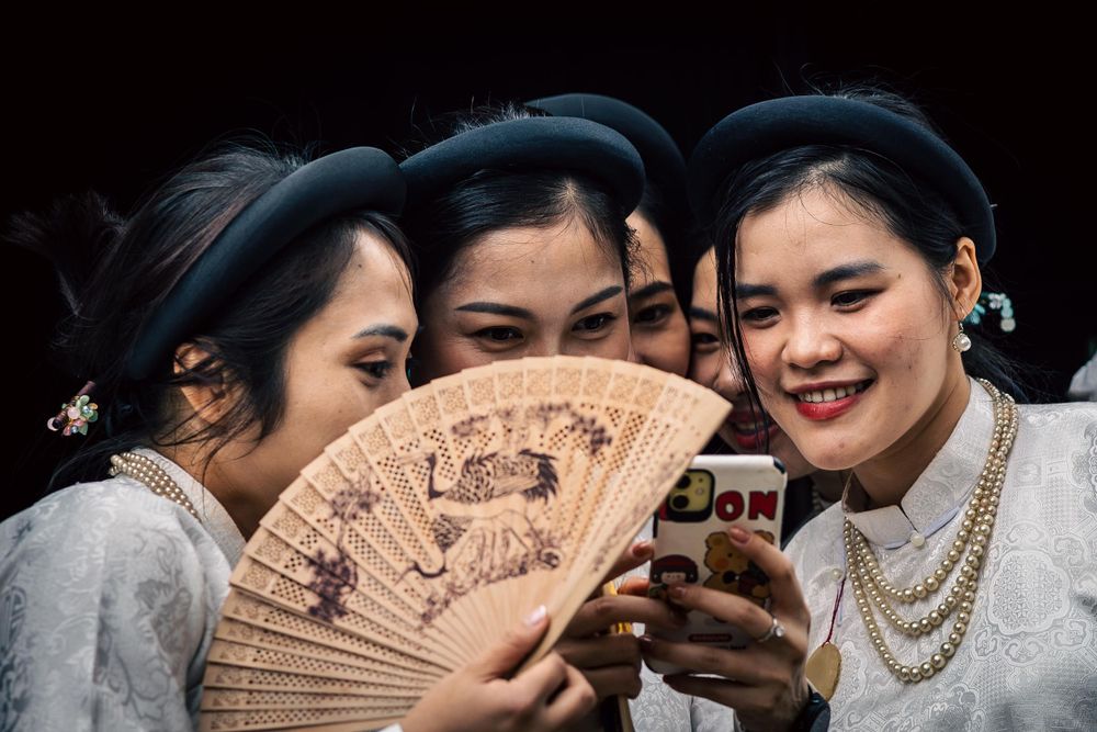 Group sharing moment with decorative fan and mobile phone.
