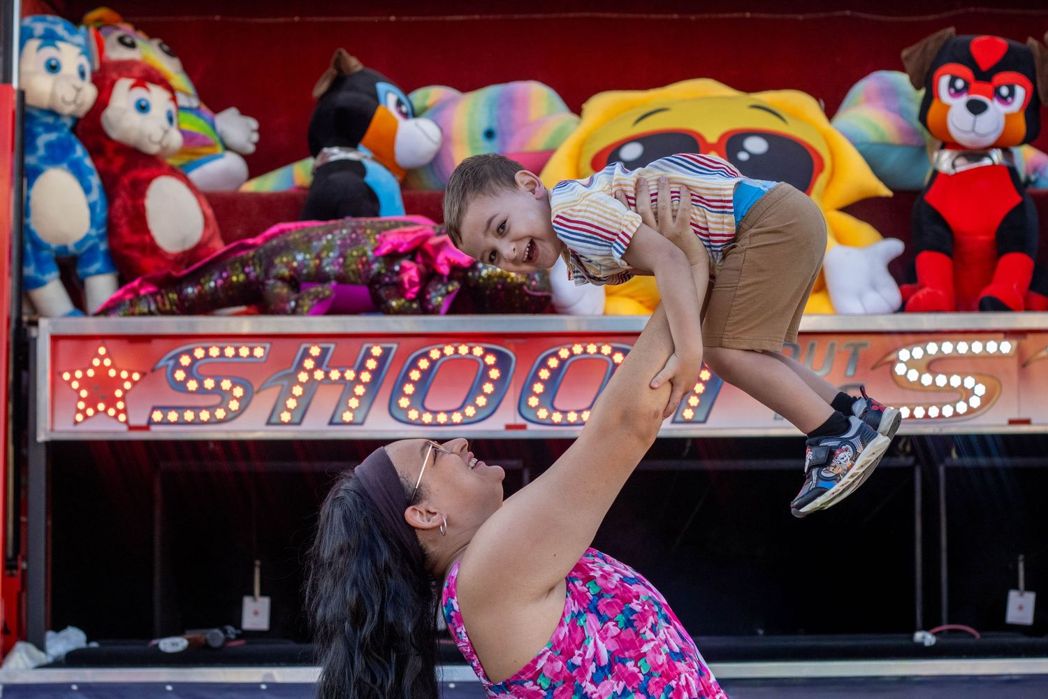 Colorful stuffed animals and carnival prizes line the shelves at a carnival game booth with bright lighting.