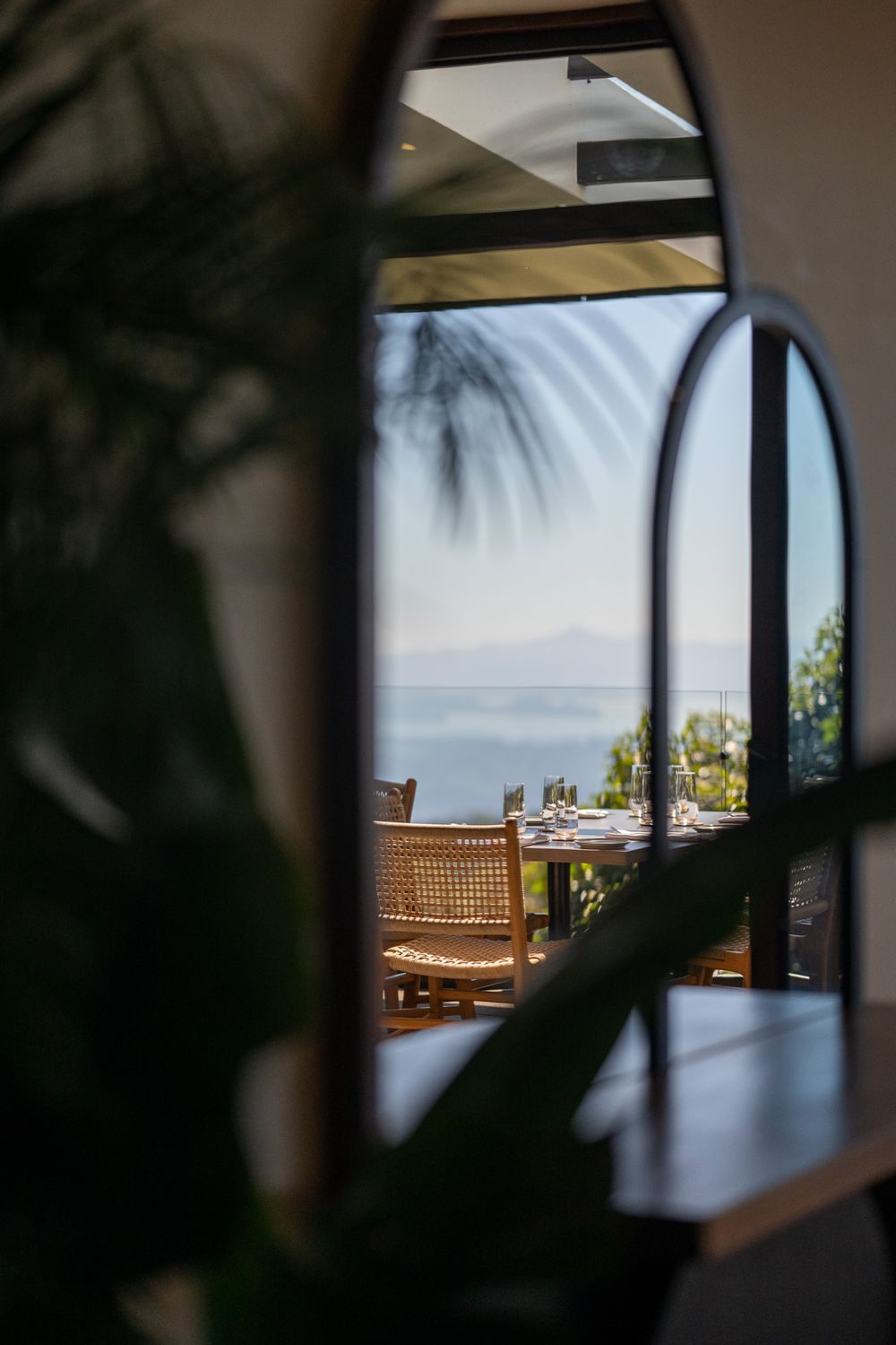 Ocean view through arched doorway with tropical plants in foreground.