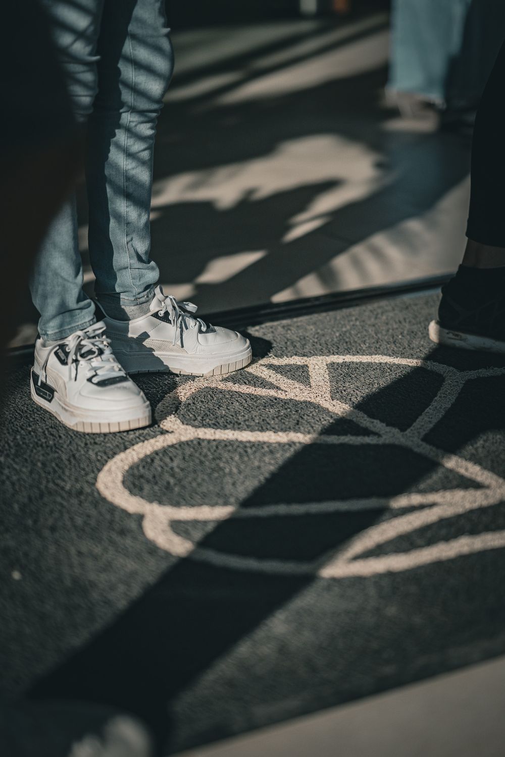 White sneakers casting geometric shadows on patterned floor.