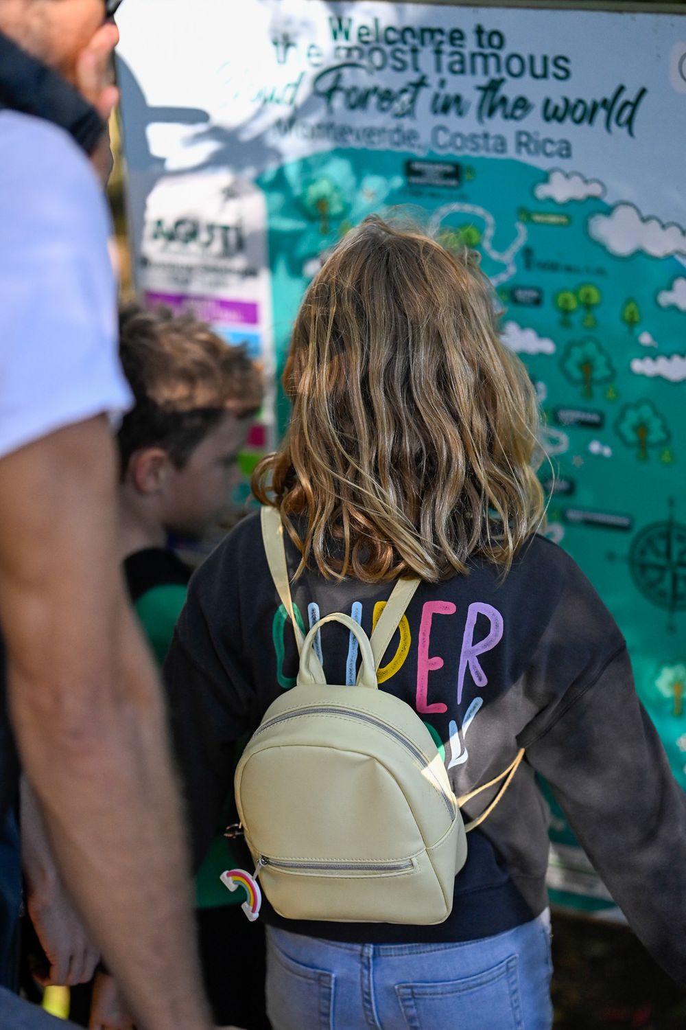 Tourist looking at colorful Costa Rica welcome sign wearing backpack and casual attire.