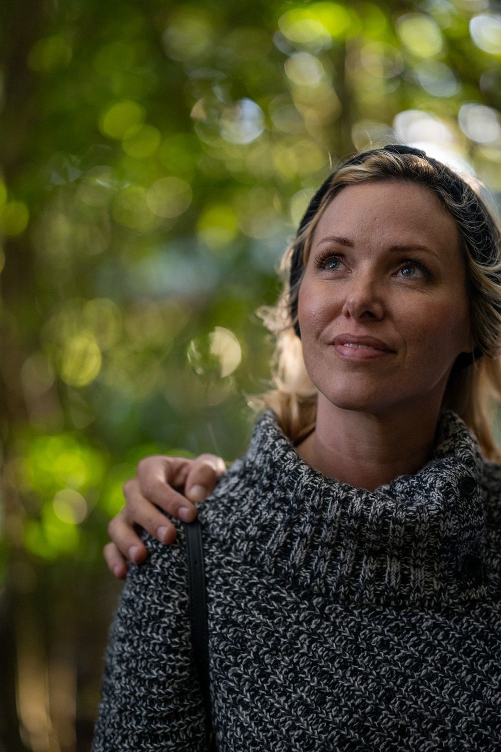 Portrait of person in knit sweater looking up thoughtfully in natural outdoor setting.