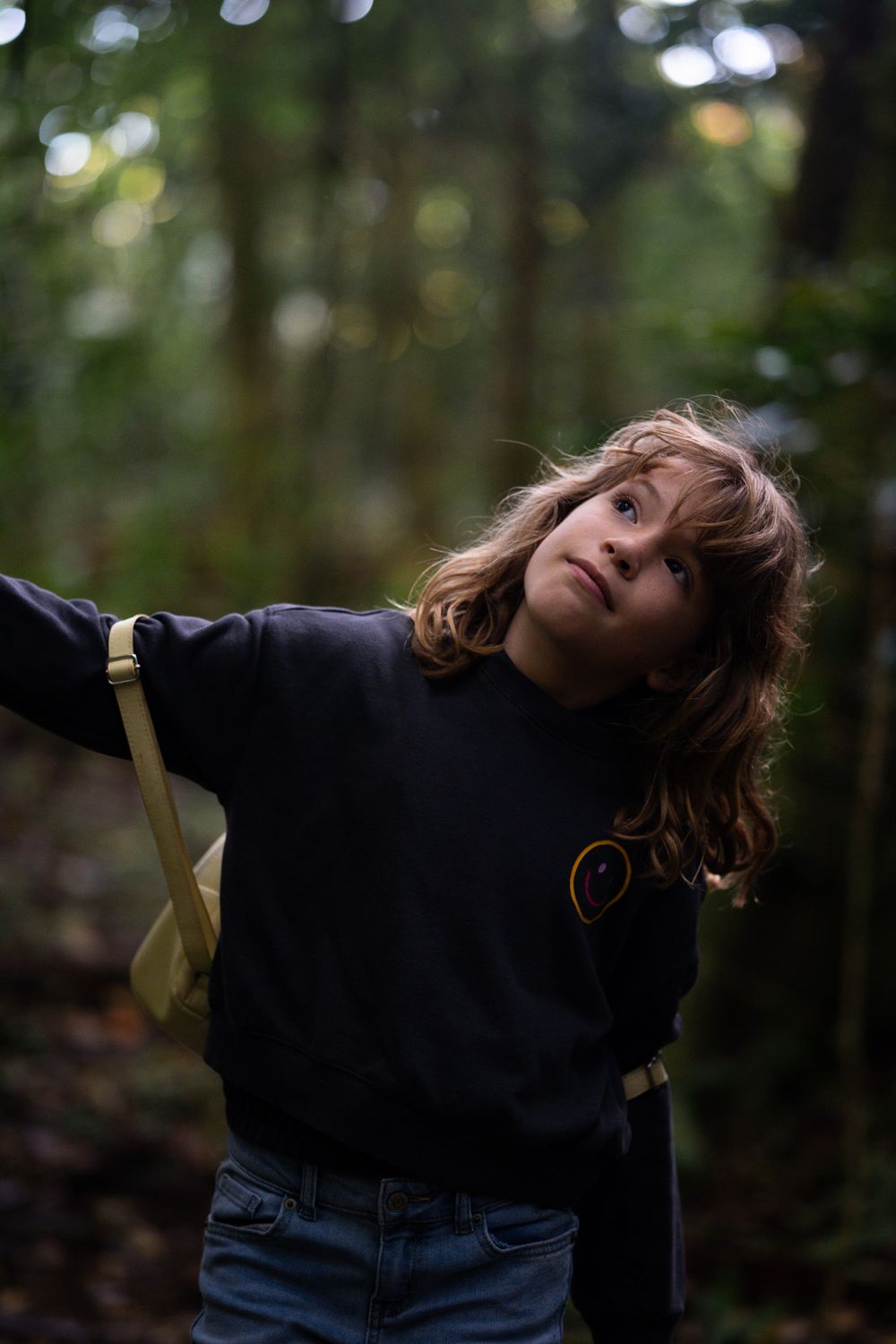 Child in navy sweater playing outdoors in wooded area with dramatic lighting.
