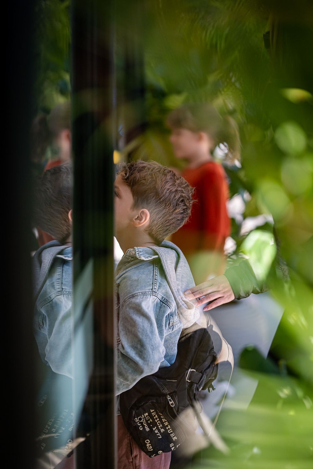 Child in denim jacket viewed through foliage.