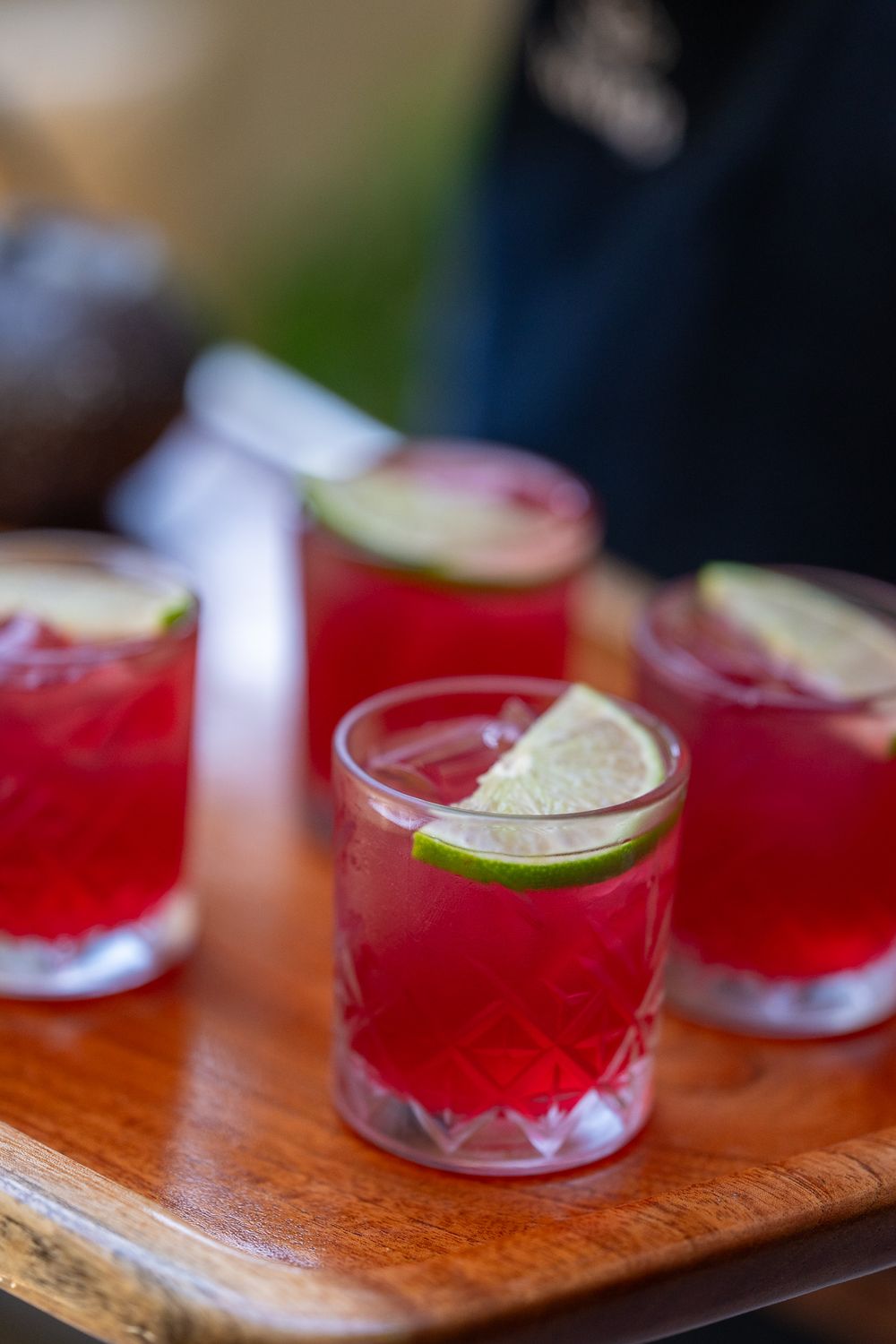Red cocktails garnished with lime slices served on wooden tray.