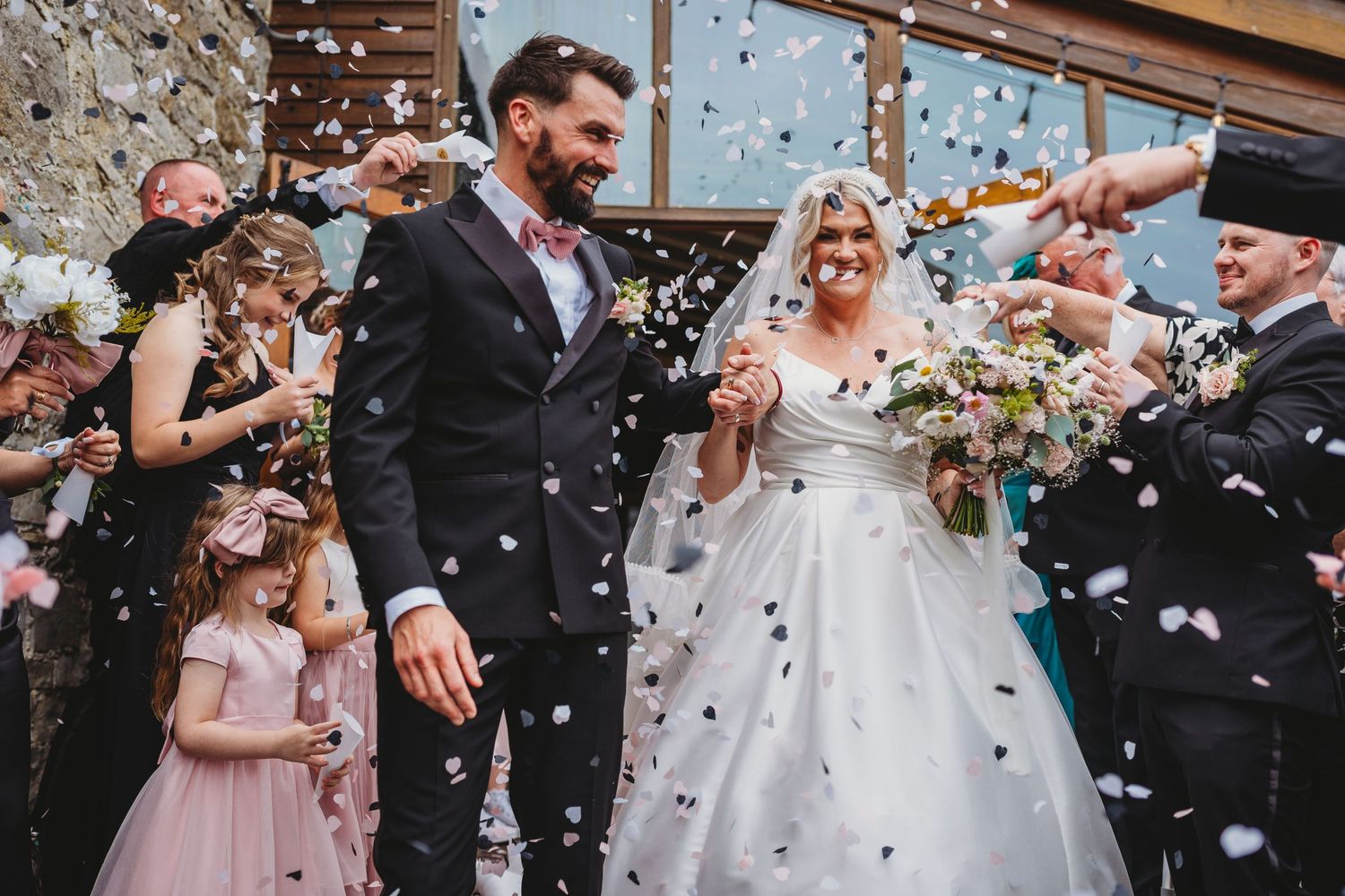 Joyful wedding party showered with confetti during outdoor celebration.