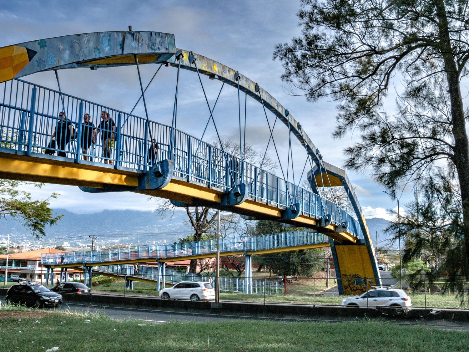 Colorful pedestrian bridge with blue and yellow arches stretching over a roadway.