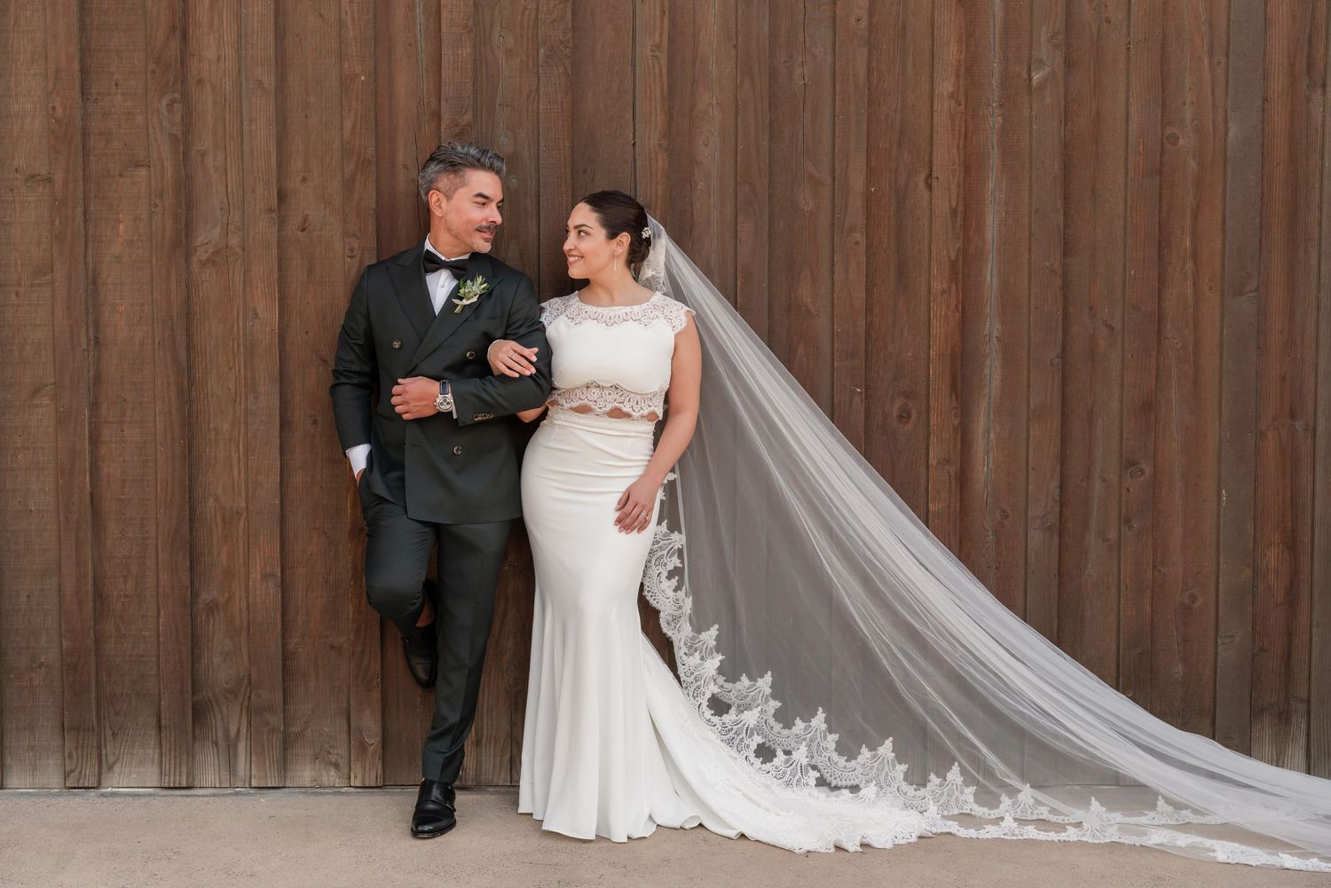 Elegant wedding portrait against wooden wall with bride wearing long lace veil and fitted white gown.