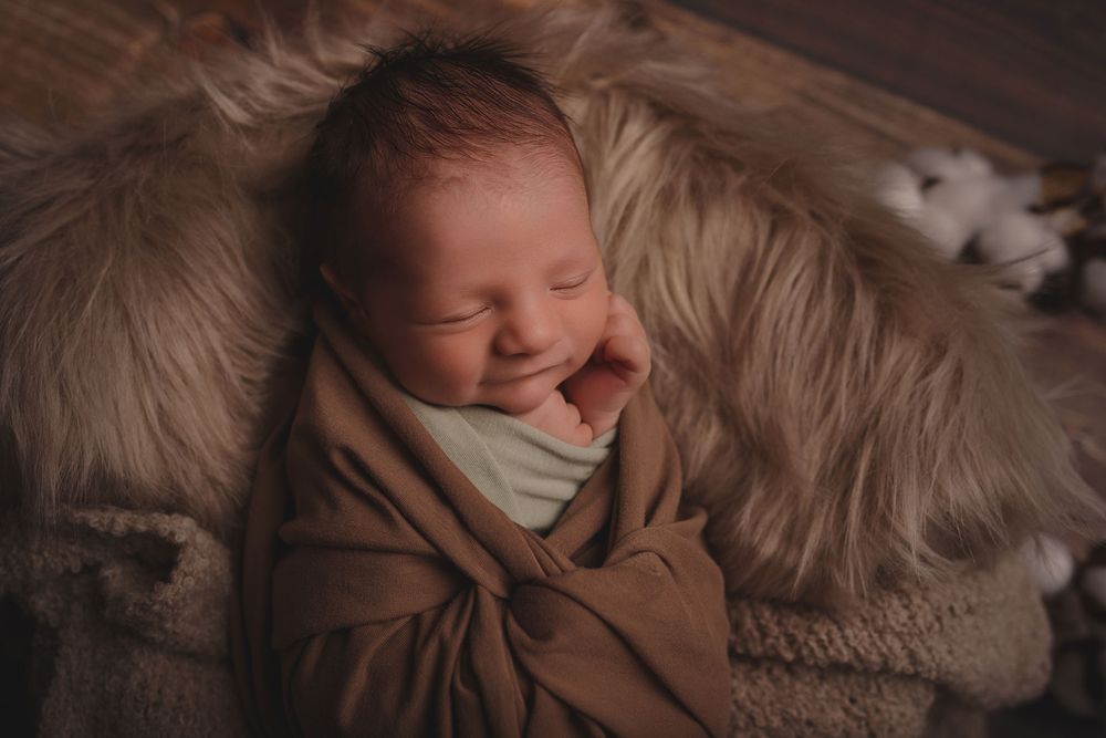 Photographie d'un bébé souriant emmailloté dans un lange coton marron, réalisée par Amandine Chiriaeff à Reims