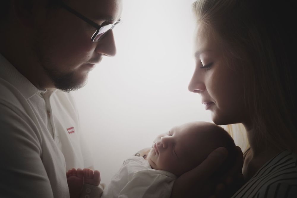 Photographie en contre jour d'un couple avec son nouveau-né réalisée par Amandine Chiriaeff dans un studio à Compiègne
