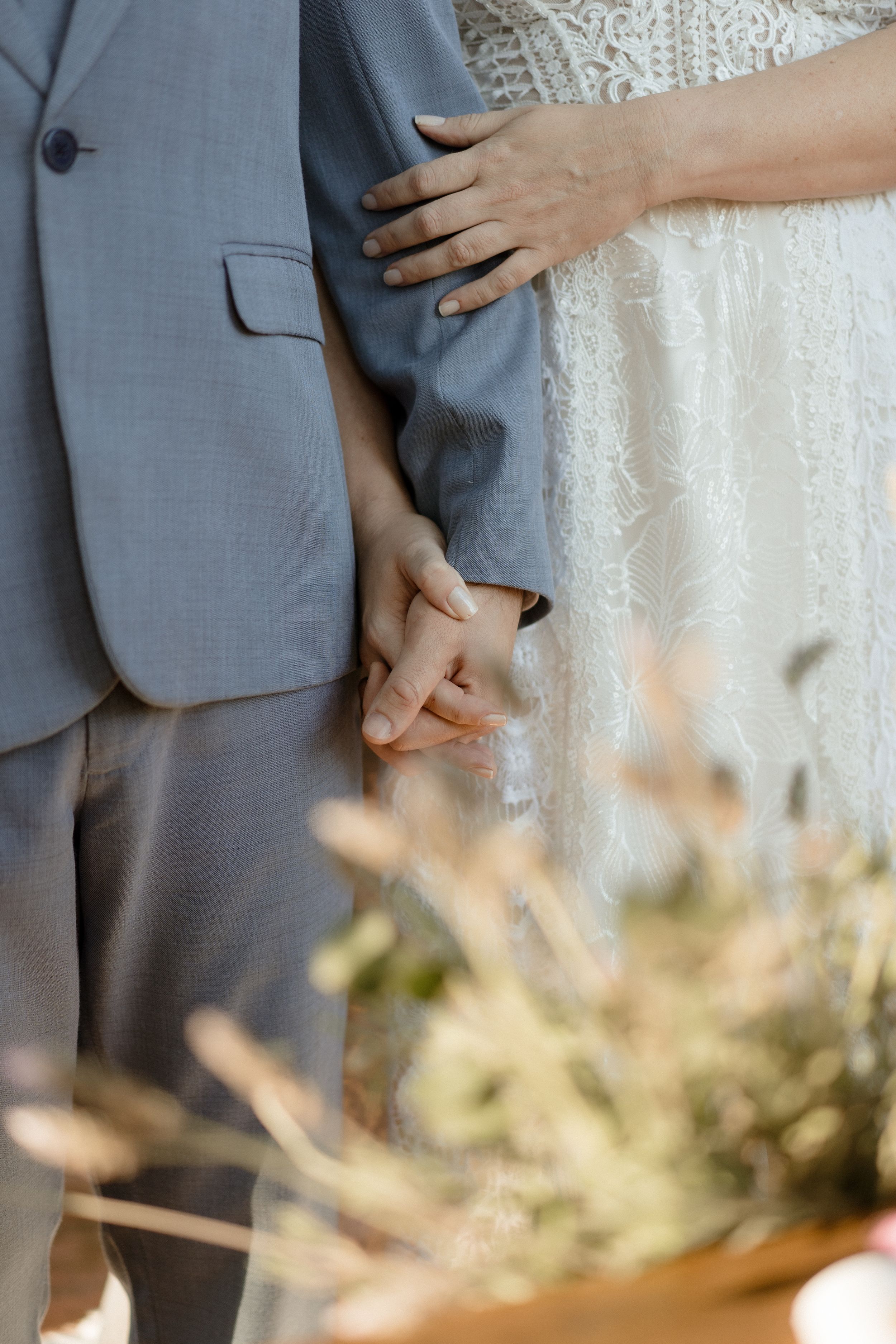 Close up detail of hands touching with wedding attire in soft natural lighting.