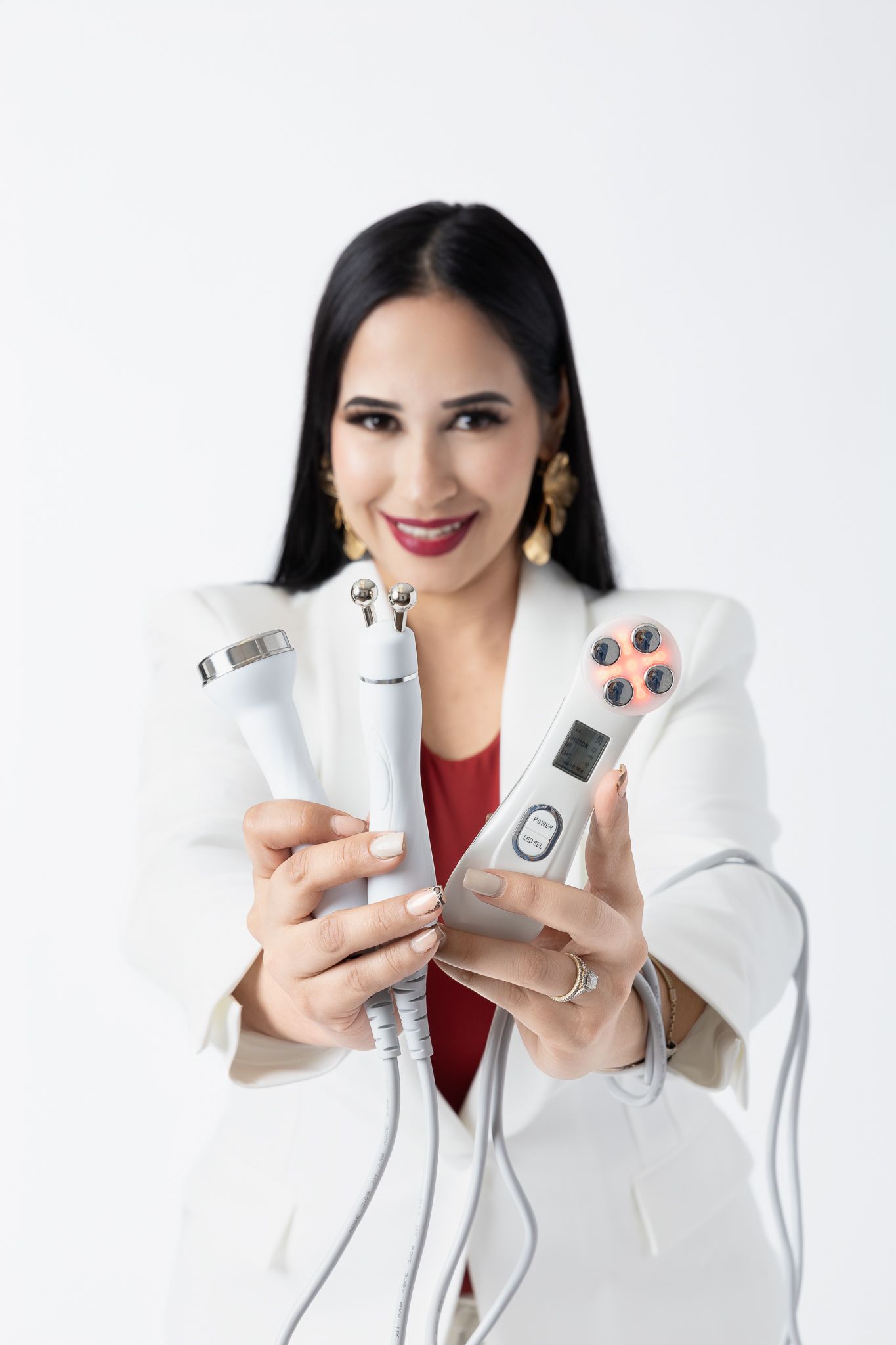 Beauty professional displaying skincare devices while wearing white blazer and red top.