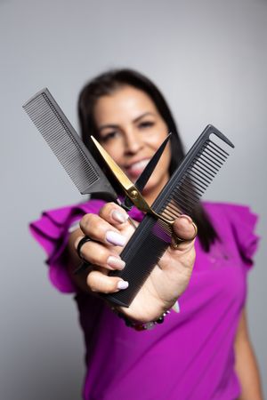 Professional holding hair styling combs in crossed position against grey background.