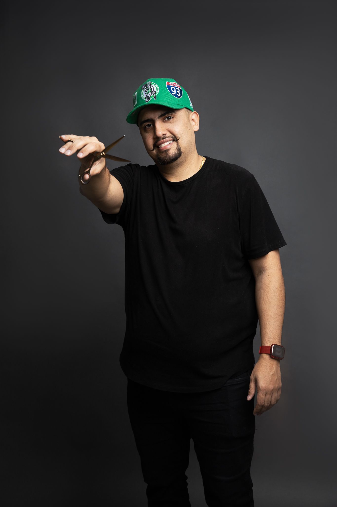 Person in black t-shirt and green baseball cap pointing against dark background.