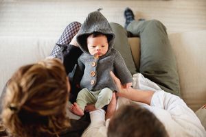 An infant resting peacefully with their guardian on comfortable grey seating cushions.