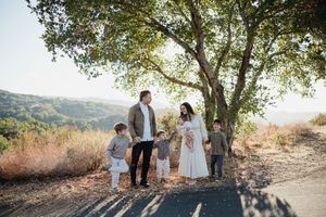 A couple shares a romantic moment on a hilltop trail surrounded by trees during golden hour.