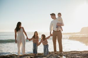 A family stands together on a beach at sunset creating silhouettes against the golden sky and ocean waves.