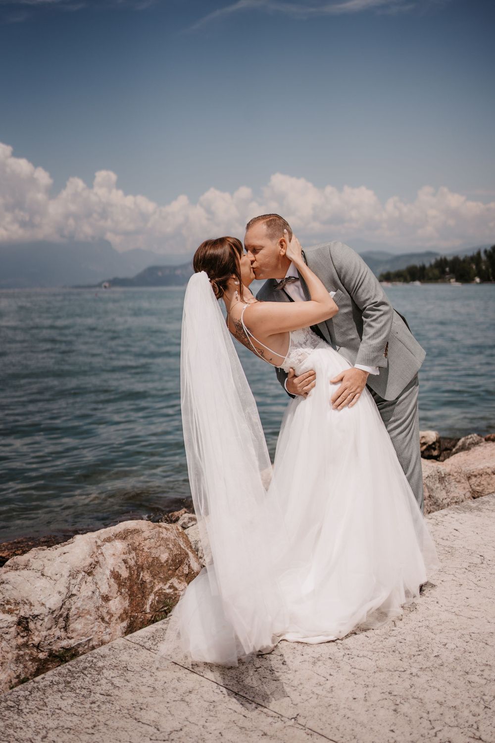 Romantic seaside wedding moment on rocky shoreline with mountains in background.