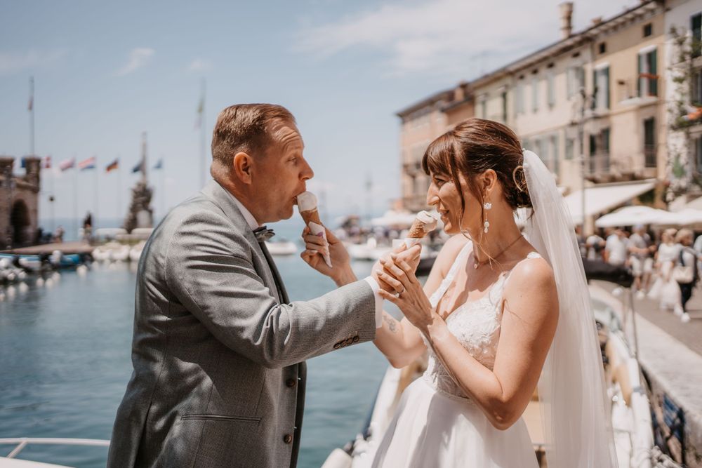 Newlyweds share a playful moment with ice cream by a seaside marina.
