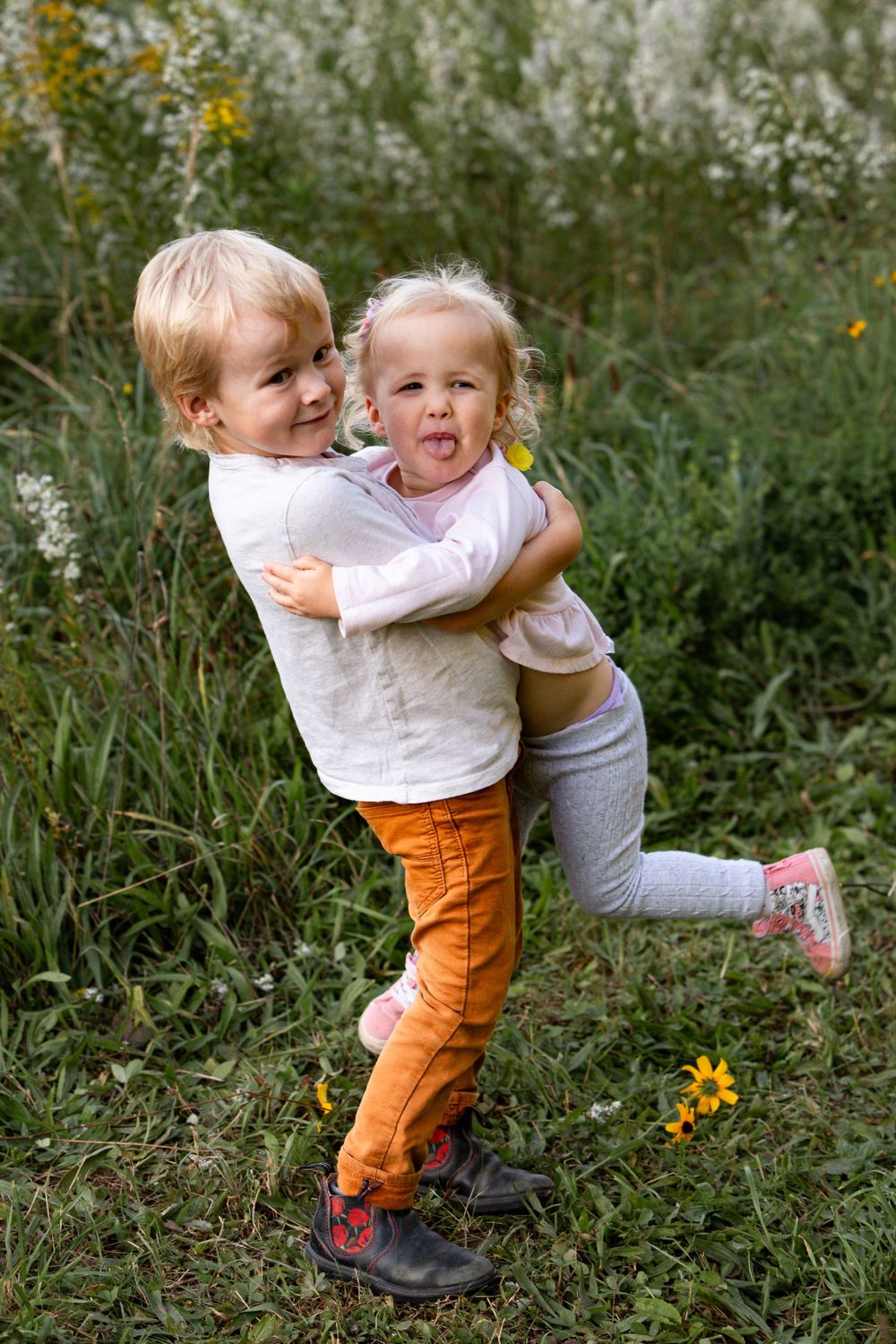 Two young children playing and hugging while standing in a field of wildflowers.
