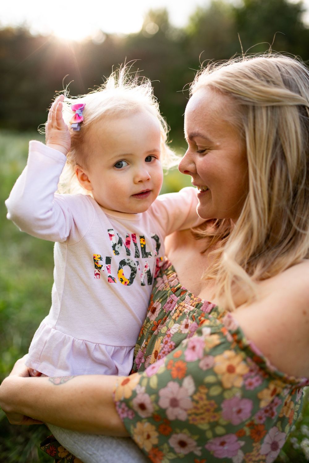 Parent and toddler share a tender moment in a sunlit field of wildflowers.