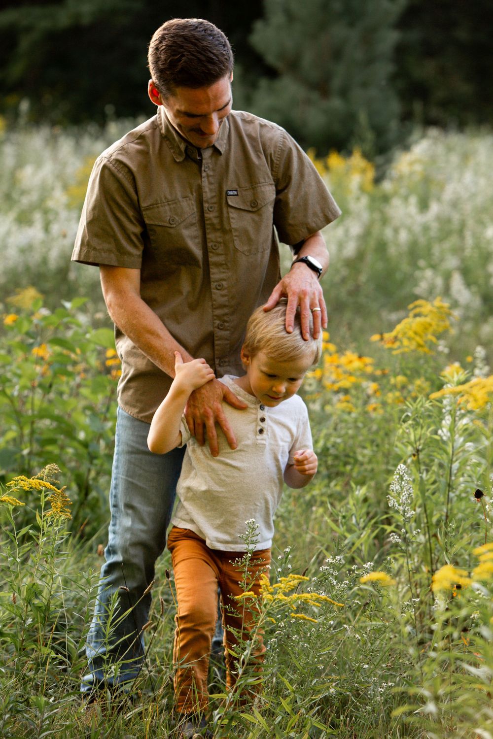 Parent guiding child through tall wildflowers in a summer meadow.