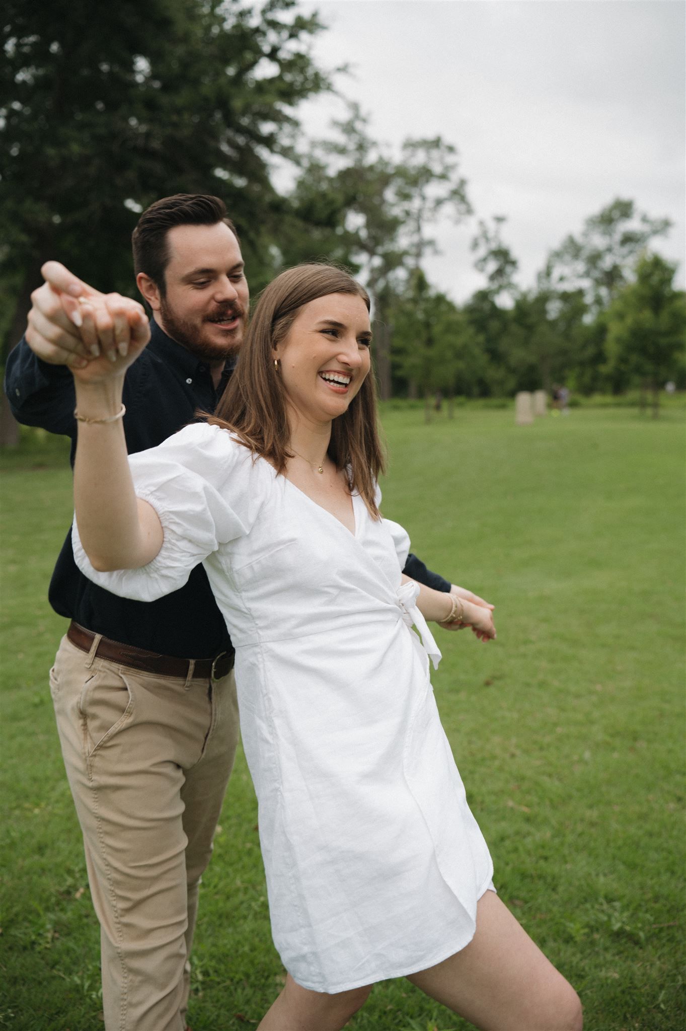 A joyful moment captured outdoors as a couple dances together in a grassy field on a cloudy day.