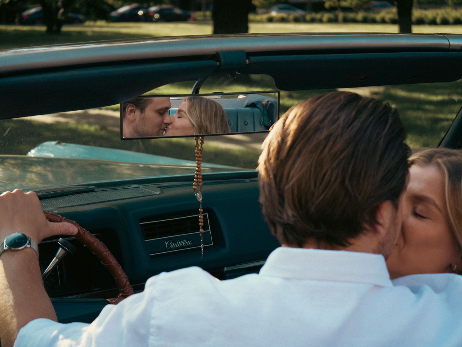 A couple sharing an intimate moment in a vintage convertible car on a sunny day.