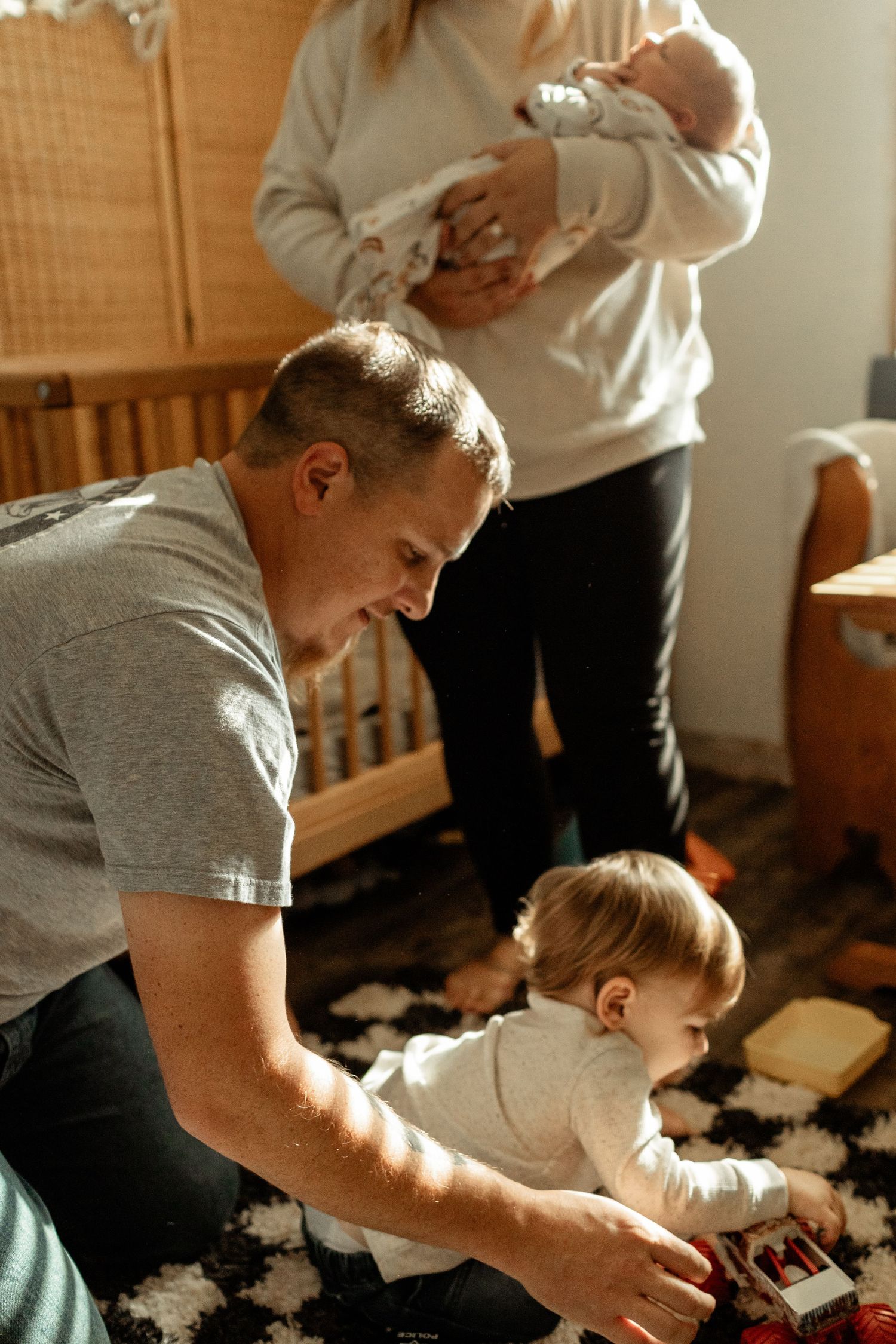 A family enjoying playtime with toys on a patterned rug in a nursery.