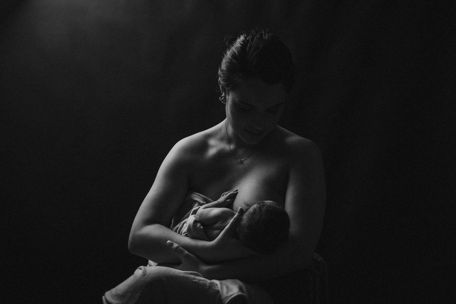 A dramatic low-light maternity portrait captured in moody shadows.
