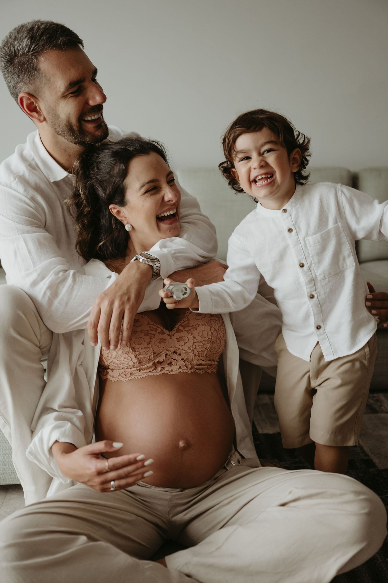 Expecting parents share tender moment with young child in bright room.