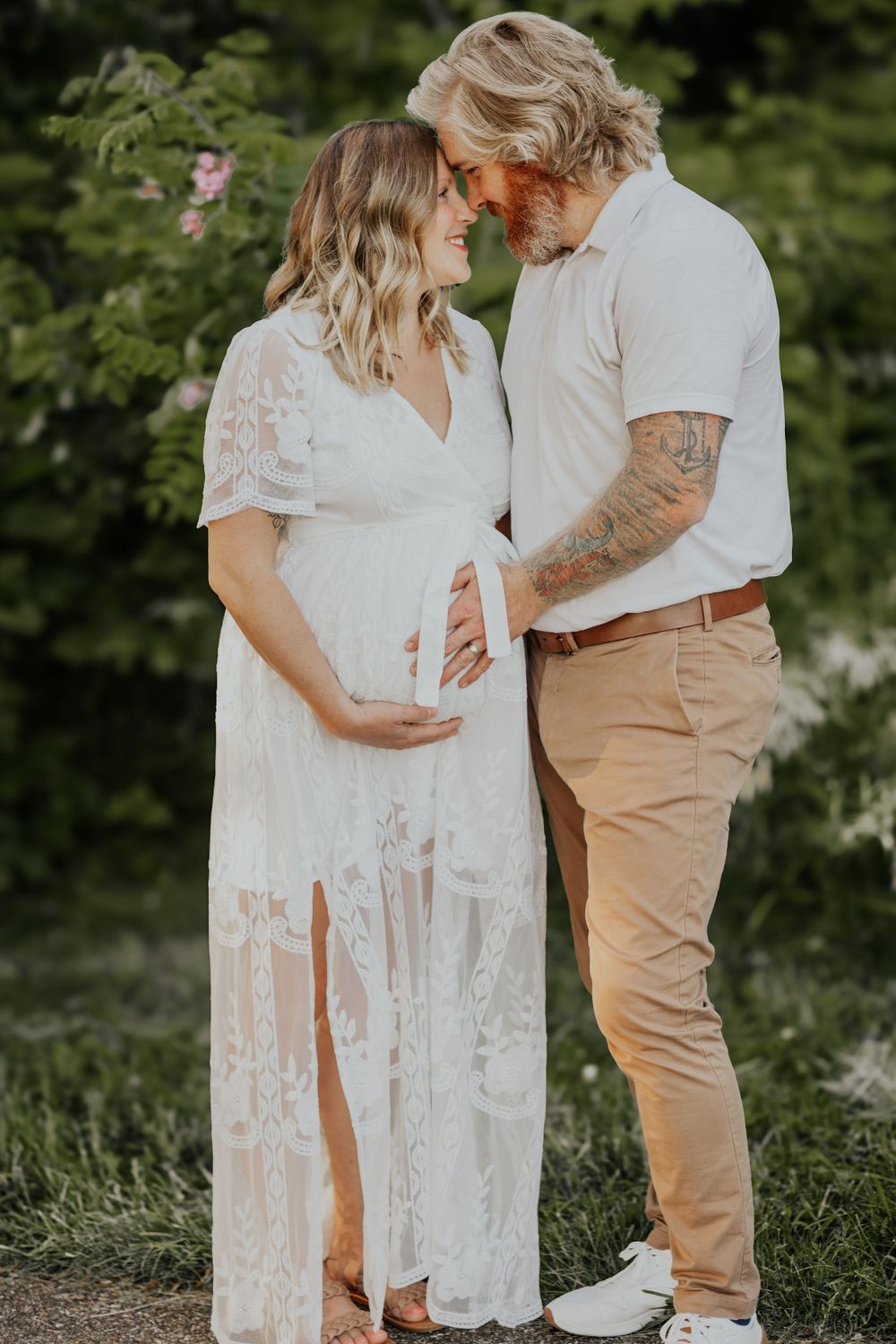 A couple in white and khaki outfits share an intimate moment outdoors during a maternity photoshoot.