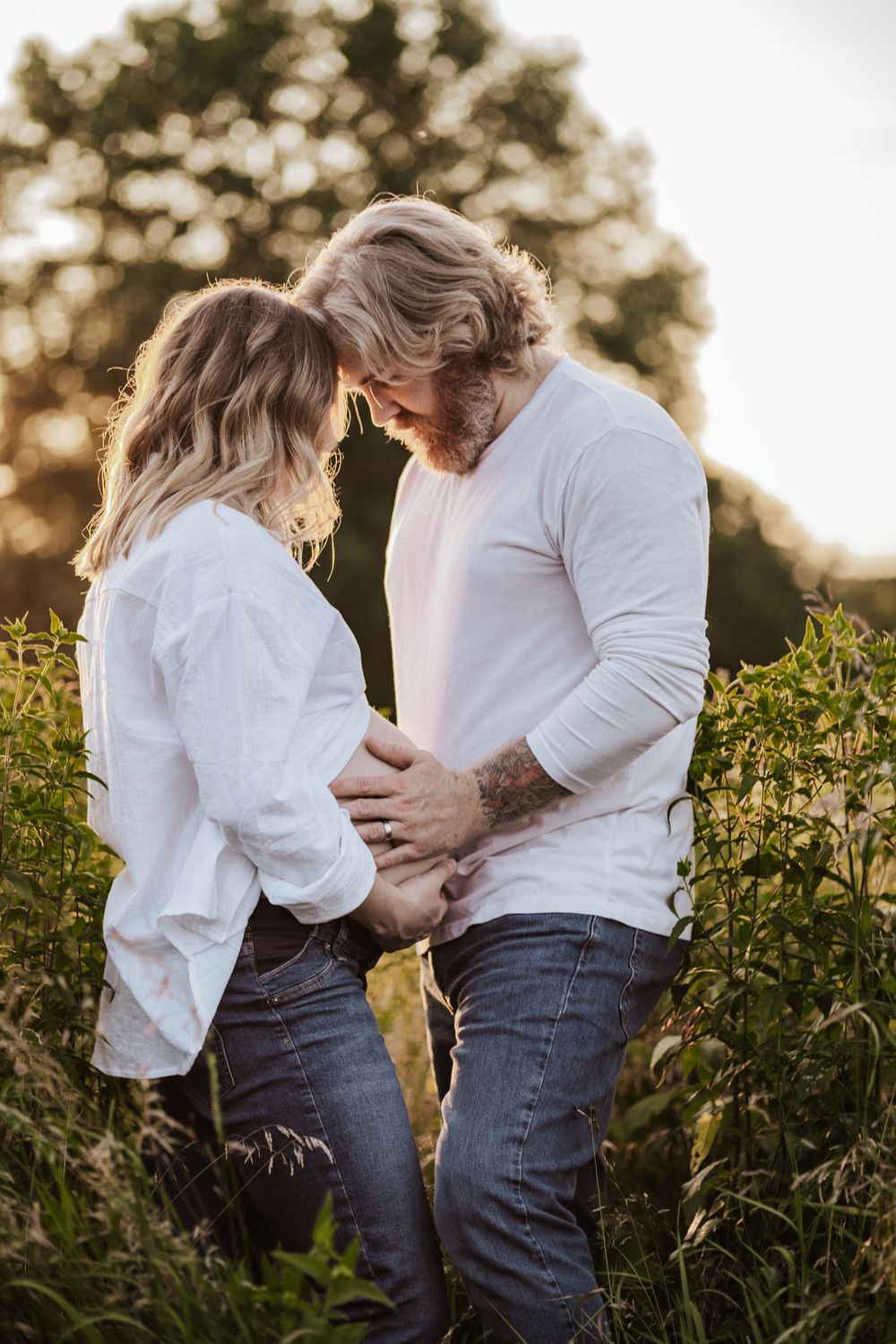 An intimate moment between a couple in white shirts standing in a sunlit field.