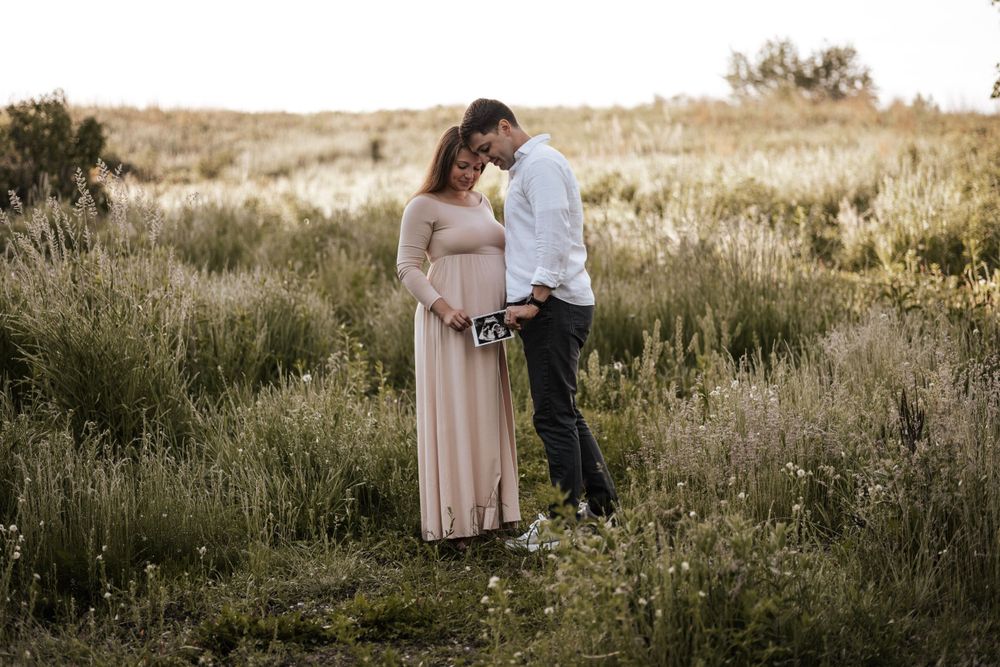 Couple embracing in golden field during sunset maternity photoshoot.