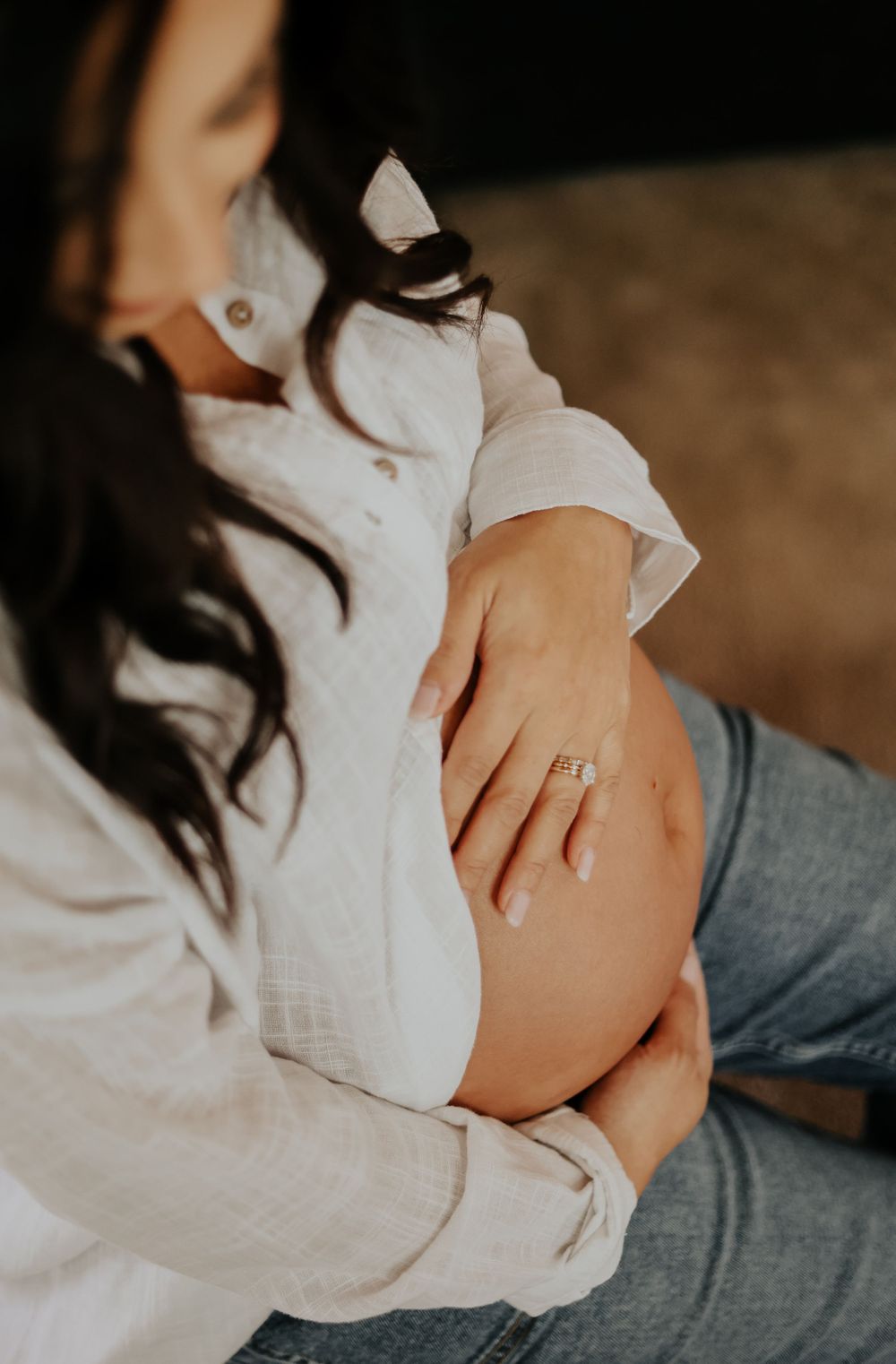 Close up of pregnant woman's belly with hands gently resting on bump.