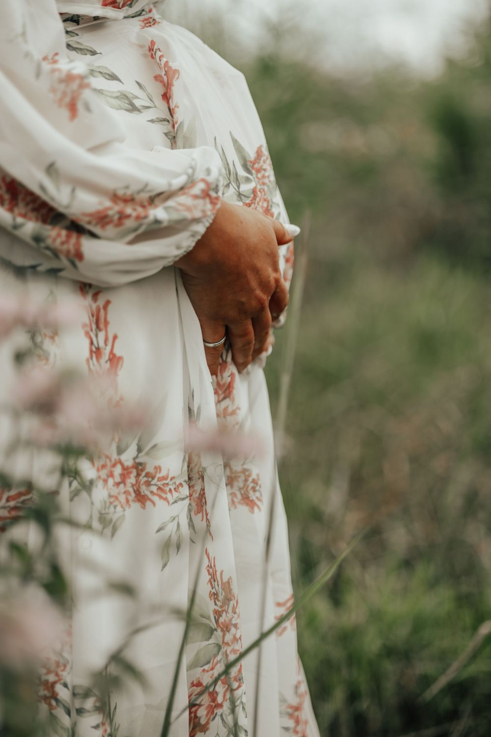 Close-up of hands cradling a pregnant belly in a floral dress against natural backdrop.