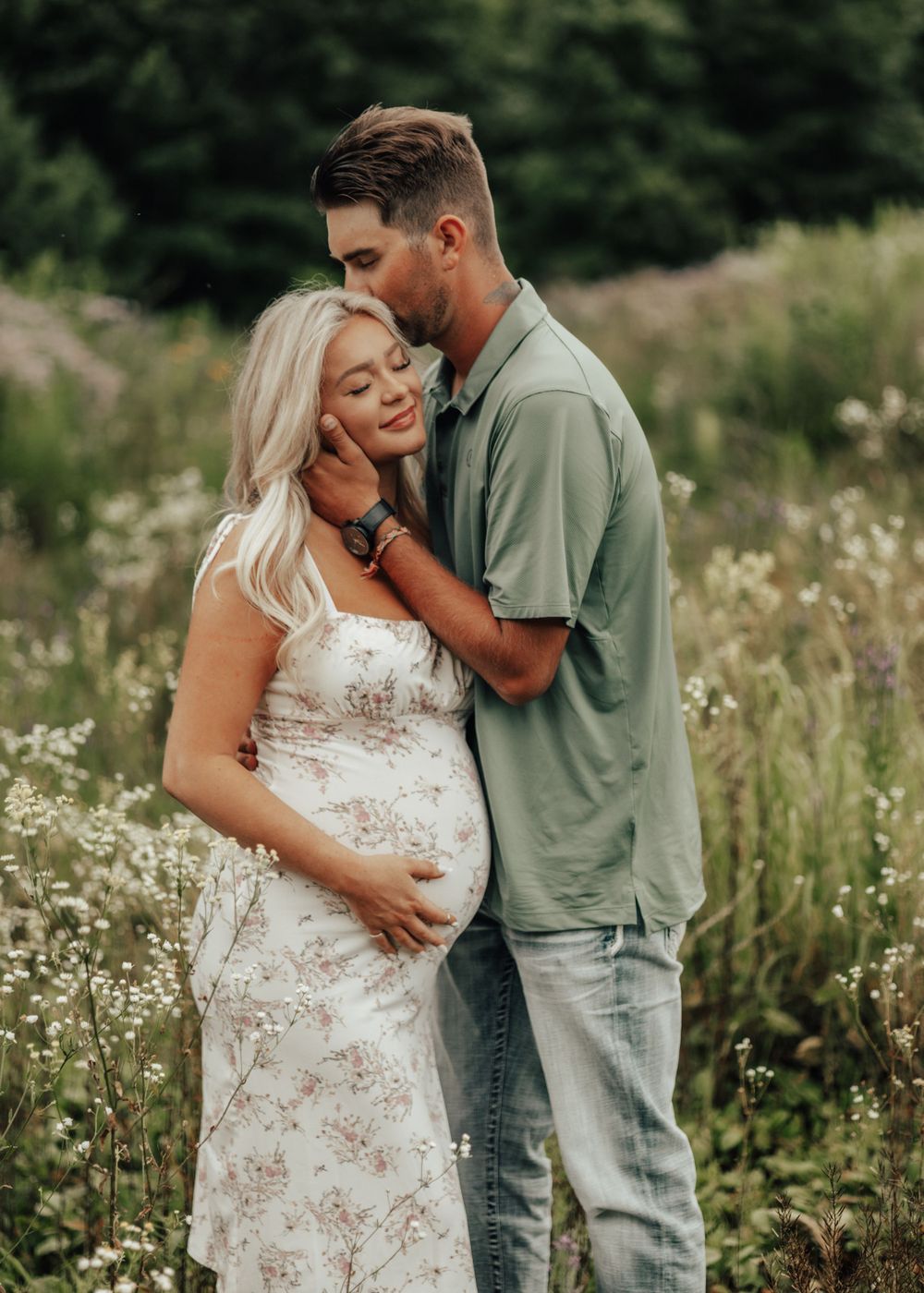 A romantic maternity photo of a couple embracing in a wildflower field at sunset.